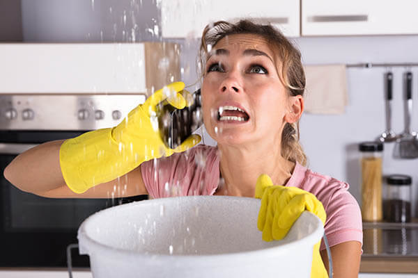 Woman catching water leaking from the ceiling with a bucket
