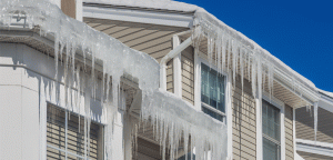 ice dam and icicles at the edge of a roof on a tan and white home