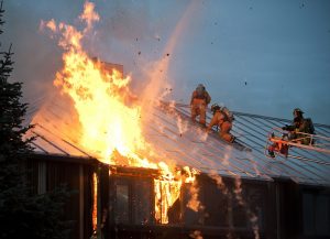 House with metal roof on fire, fire fighters on roof working