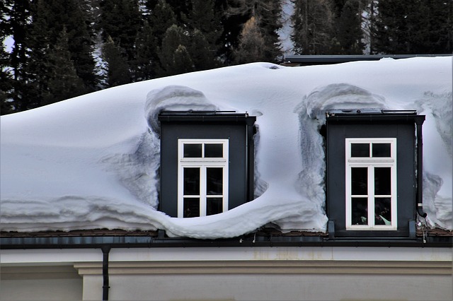 Closeup of roof with heavy snow accumulation around two dormers.
