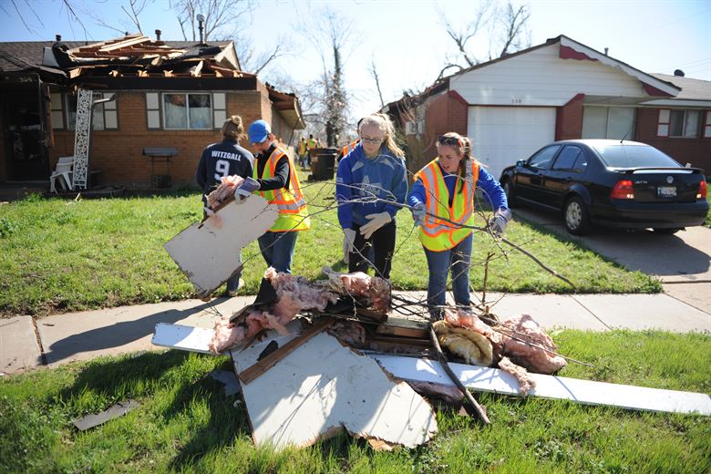 people in yard cleaning up after tornado damages homes