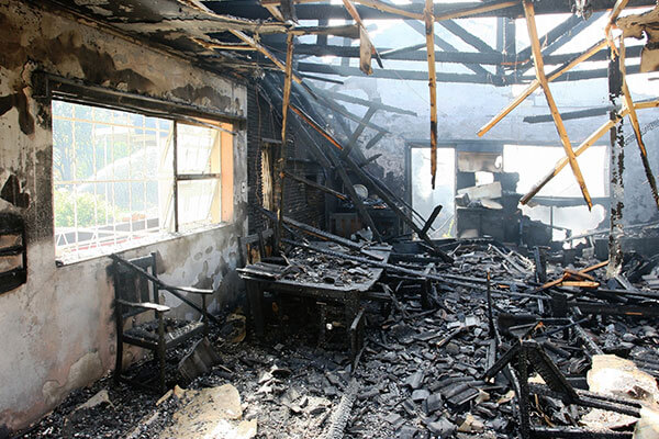 Fire damage restoration scene showing a heavily burned room with charred debris and exposed framing after a fire
