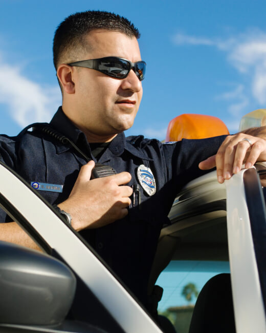 Male security using two-way radio while leaning on car Security guard services near me Los Angeles